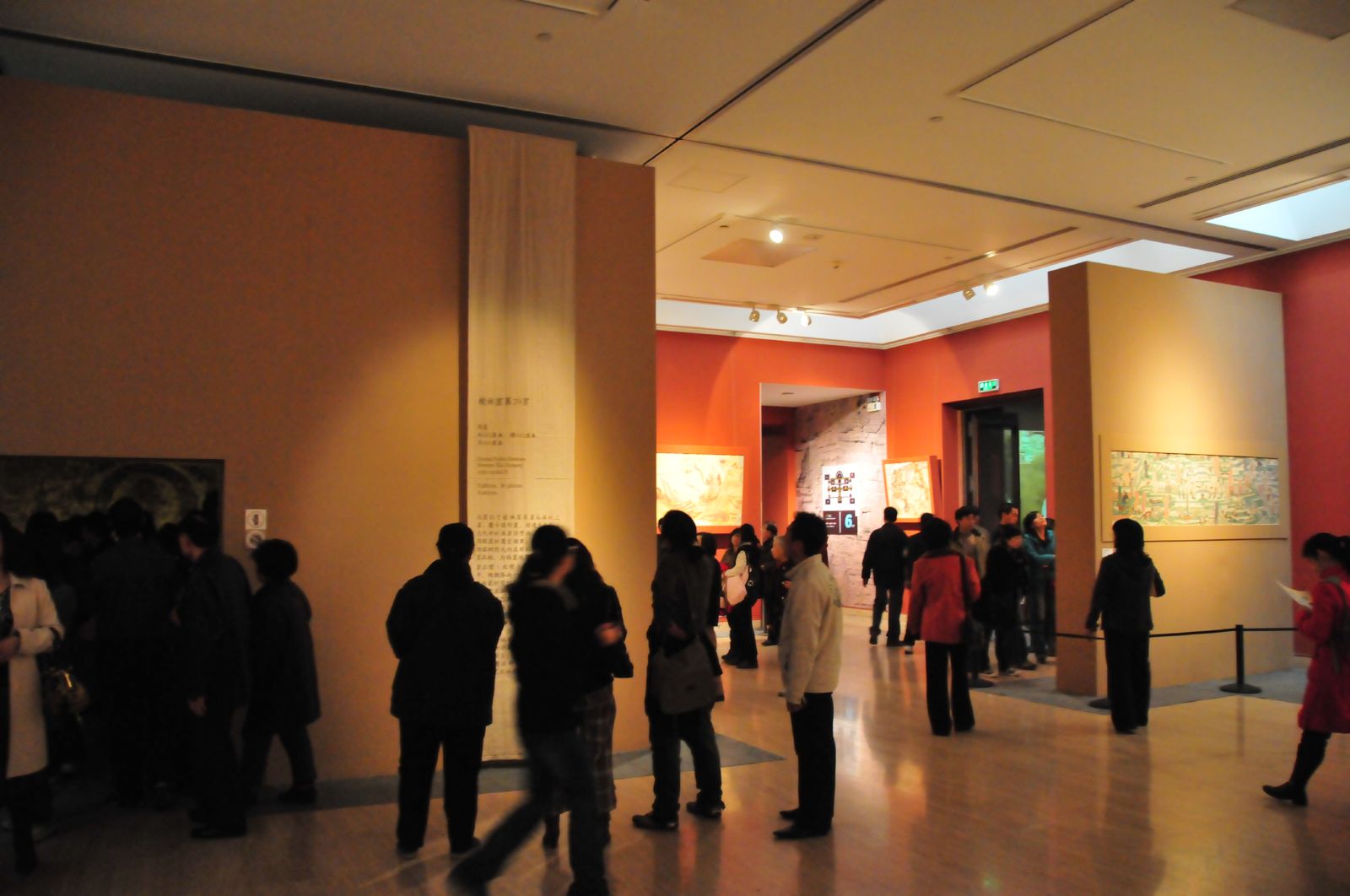 A crowded temporary exhibition hall at the National Art Museum of China, visitors viewing framed works on red-toned walls