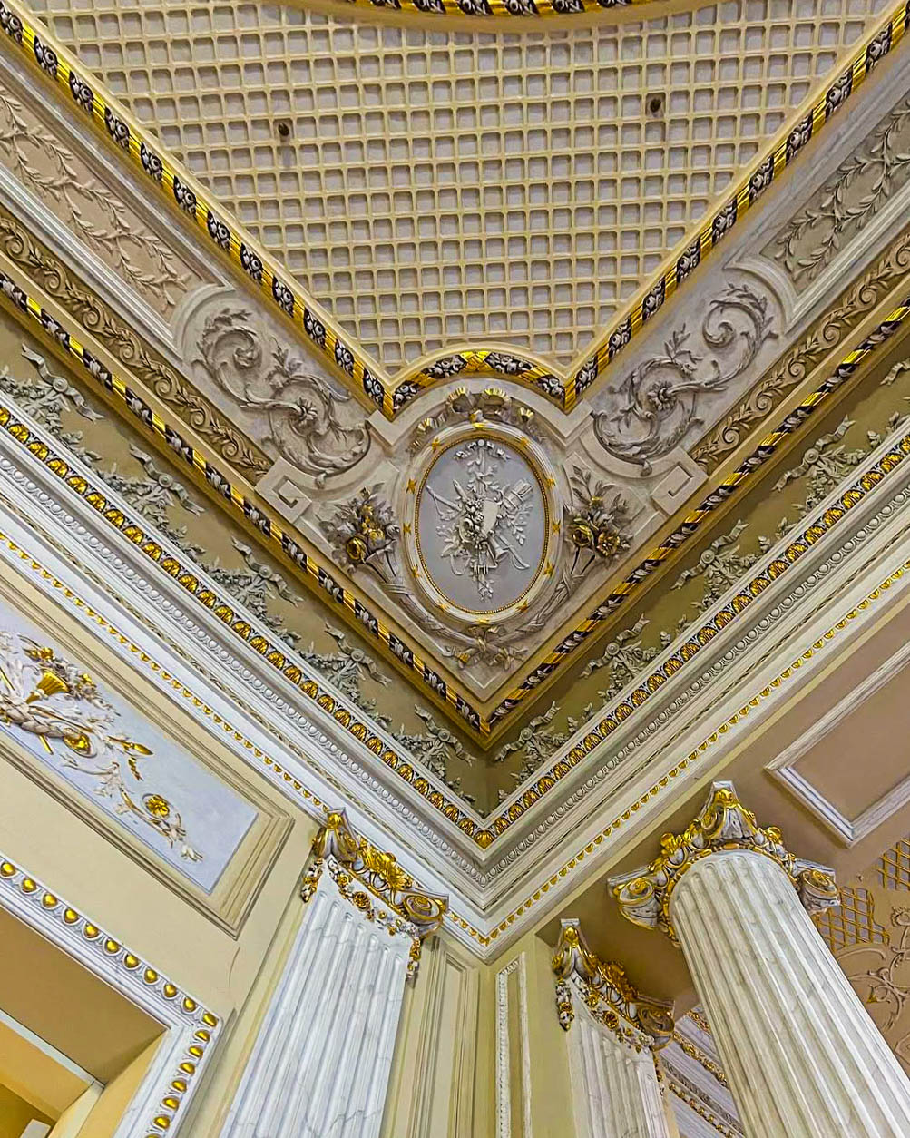 A close view of an ornate gilded and carved plaster ceiling corner above fluted Ionic columns