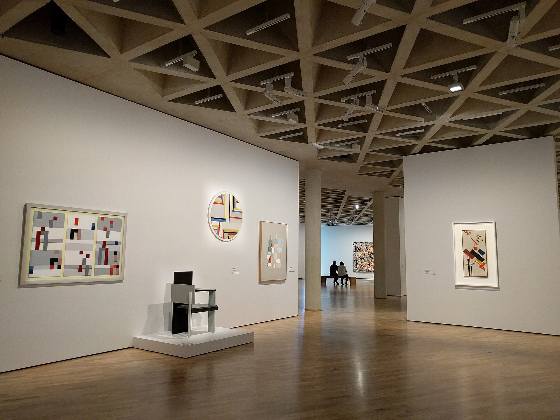 A top-lit international art gallery on the uppermost level of the National Gallery of Australia, hung with modernist paintings under a triangular waffle-slab ceiling