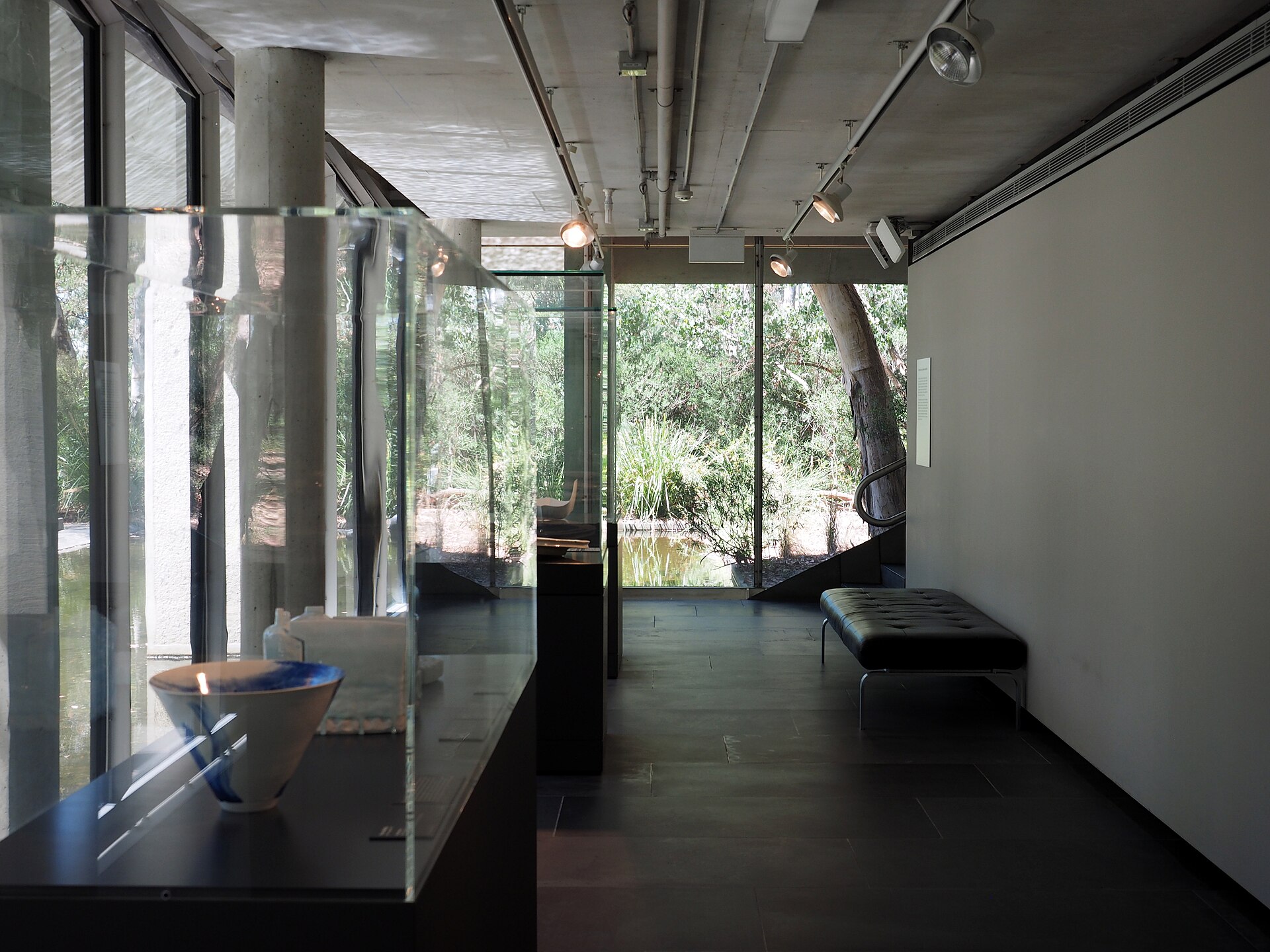 The glass-walled Water Gallery on the lowest level of the National Gallery of Australia, with a display case in the foreground and a pond visible through the windows