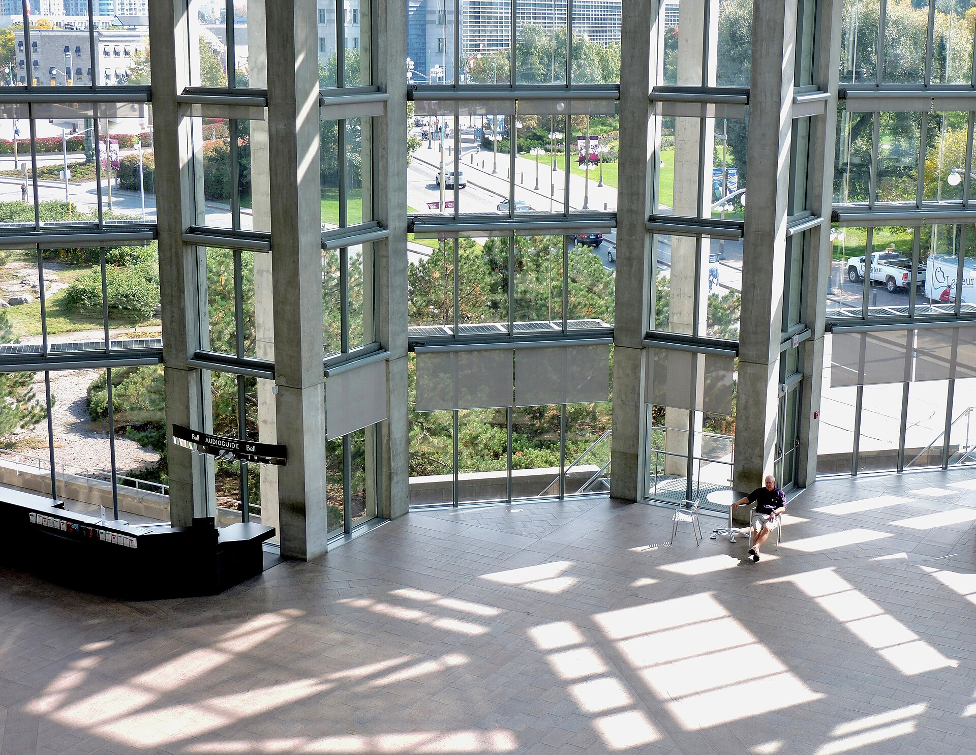 A high glass-walled hall with tall concrete columns, wide floor-to-ceiling windows and a view over the surrounding grounds