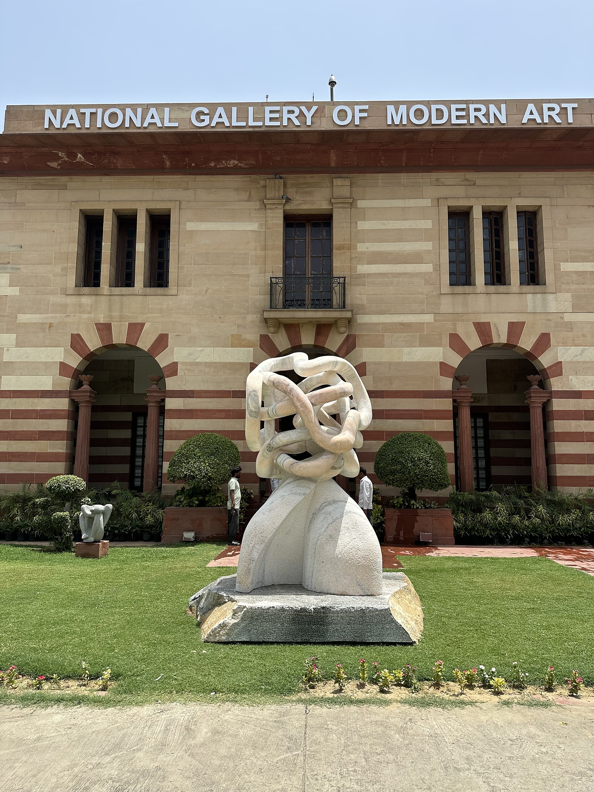 A modern stone sculpture on the lawn in front of the National Gallery of Modern Art building