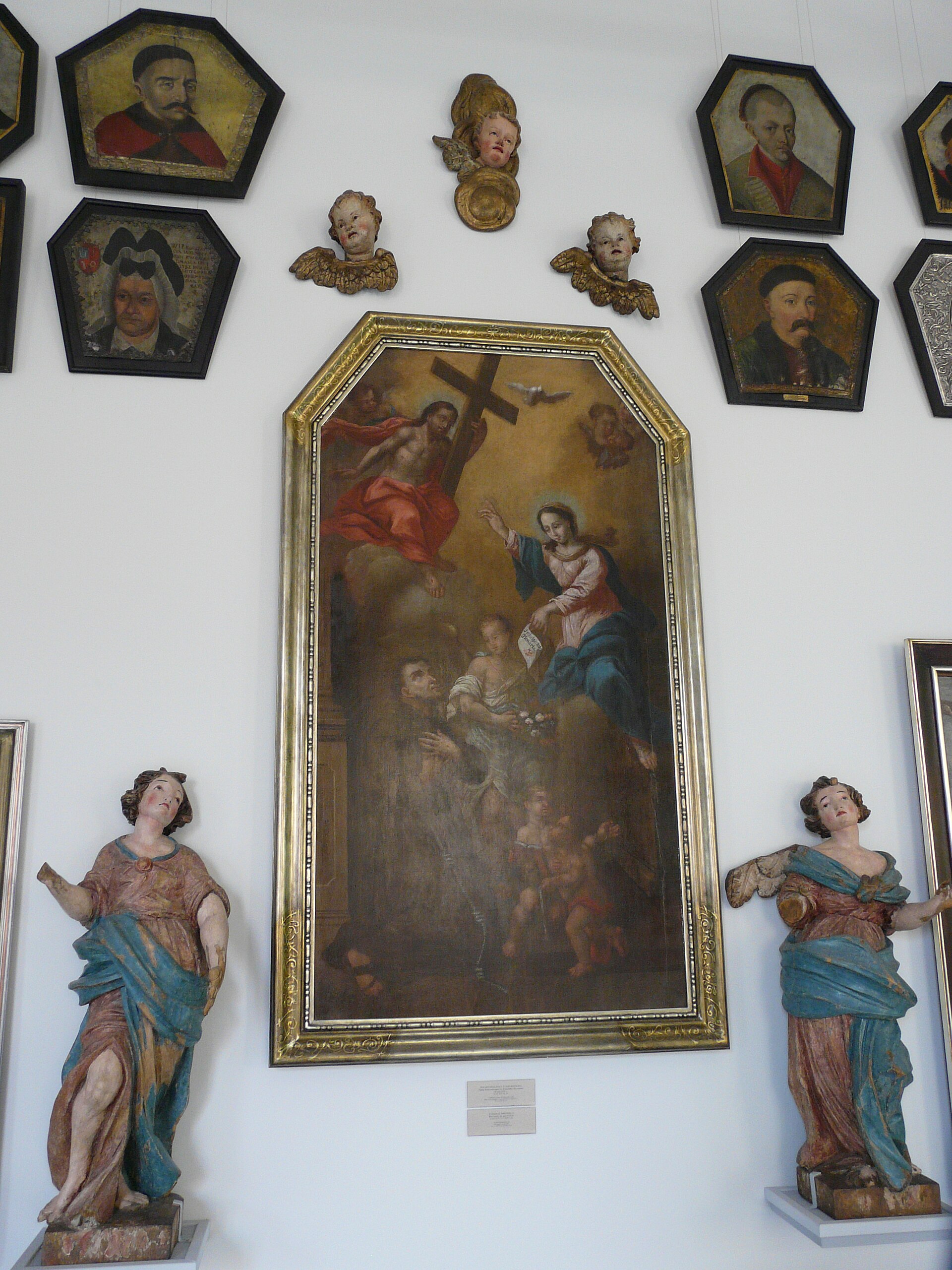 Coffin portraits flanking a Baroque religious painting of the Virgin and two gilded angel busts, in a gallery of the National Museum in Poznan