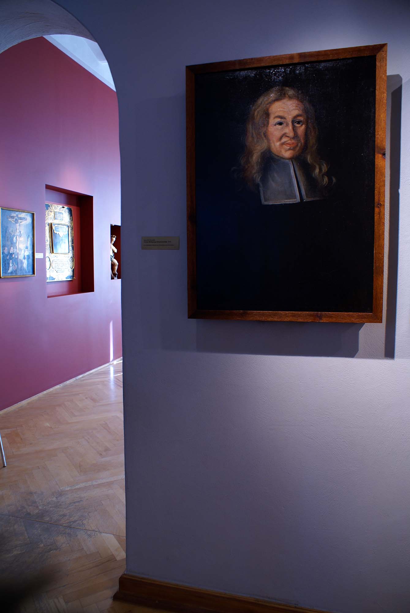 A quiet lavender-walled painting gallery with a dark-ground portrait in a wooden frame, inside the National Museum in Wroclaw