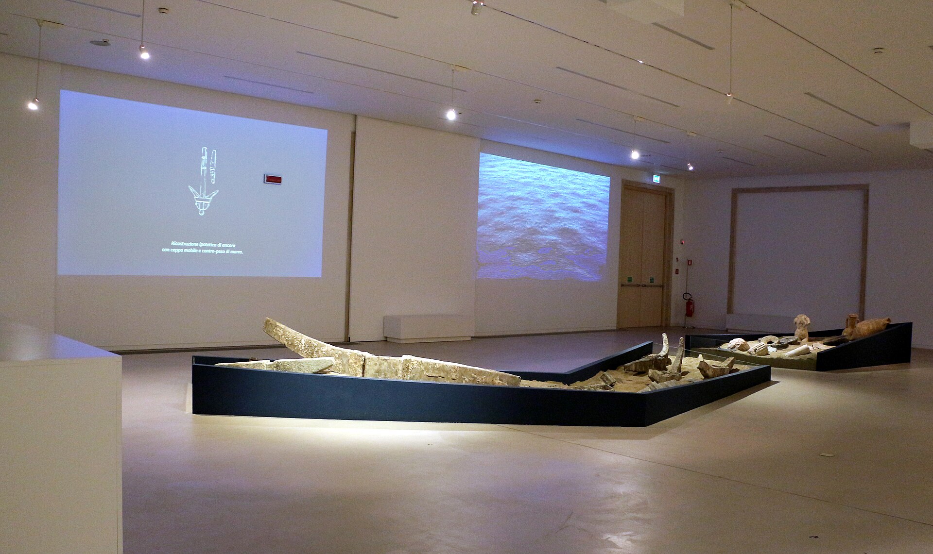 The underwater-archaeology gallery on Level D, showing timbers from an ancient wreck displayed in a low case beneath projected reconstruction diagrams, in the run of rooms leading to the Riace Bronzes hall