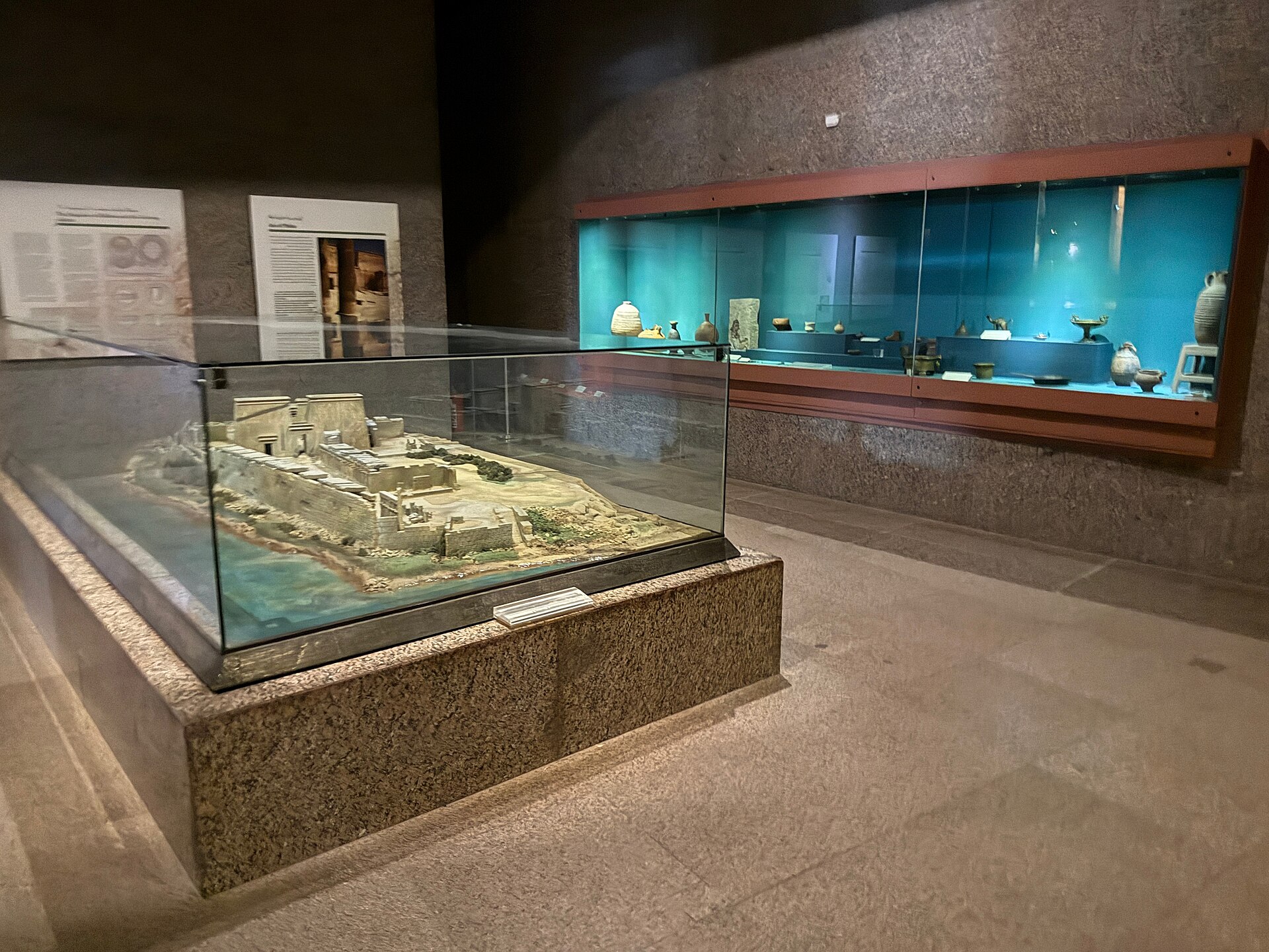 A scale model of an archaeological site beside lit display cases of pottery and small objects