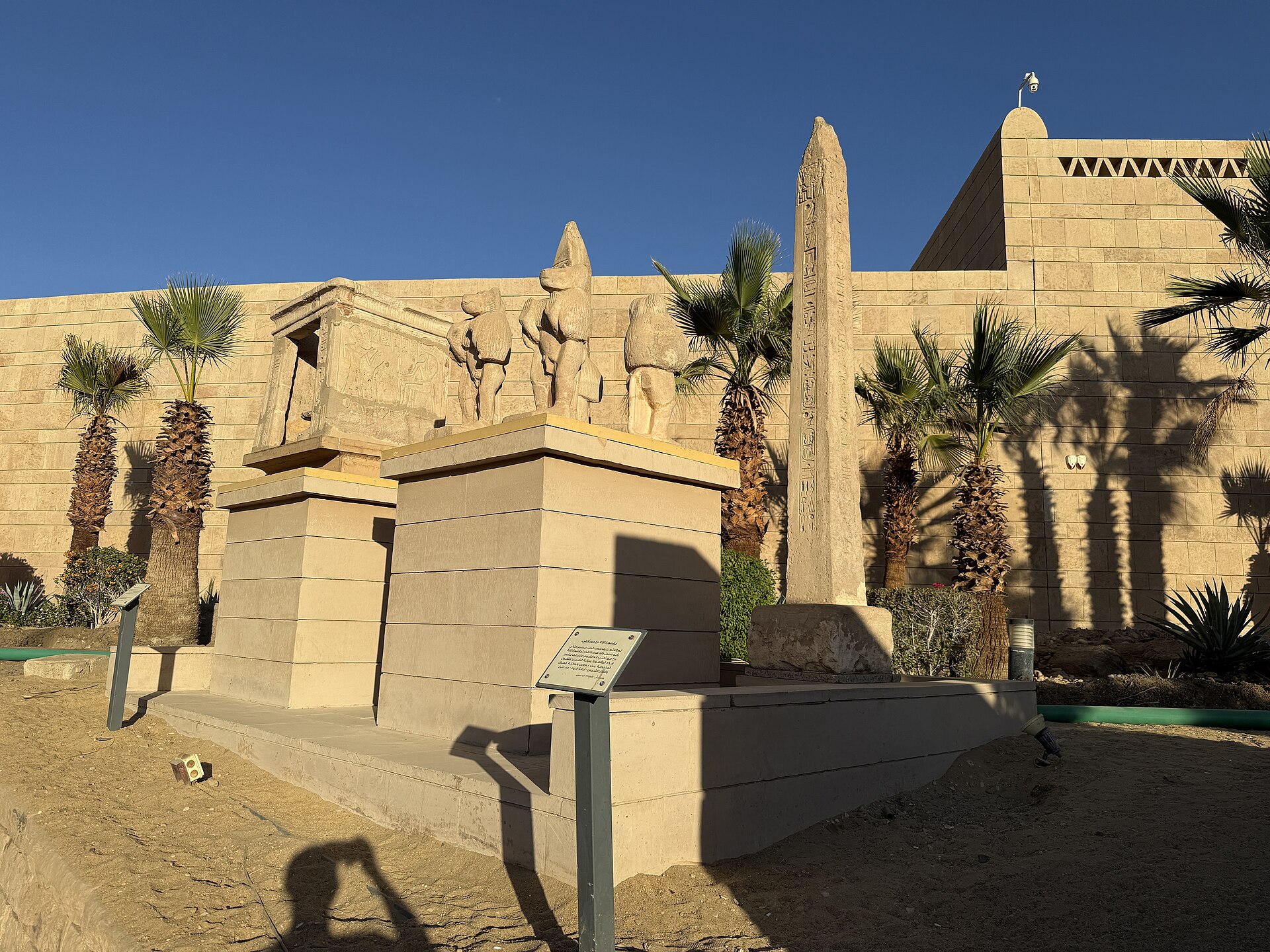 An outdoor sculpture garden with a carved relief block and an obelisk, the museum's sandstone wall behind