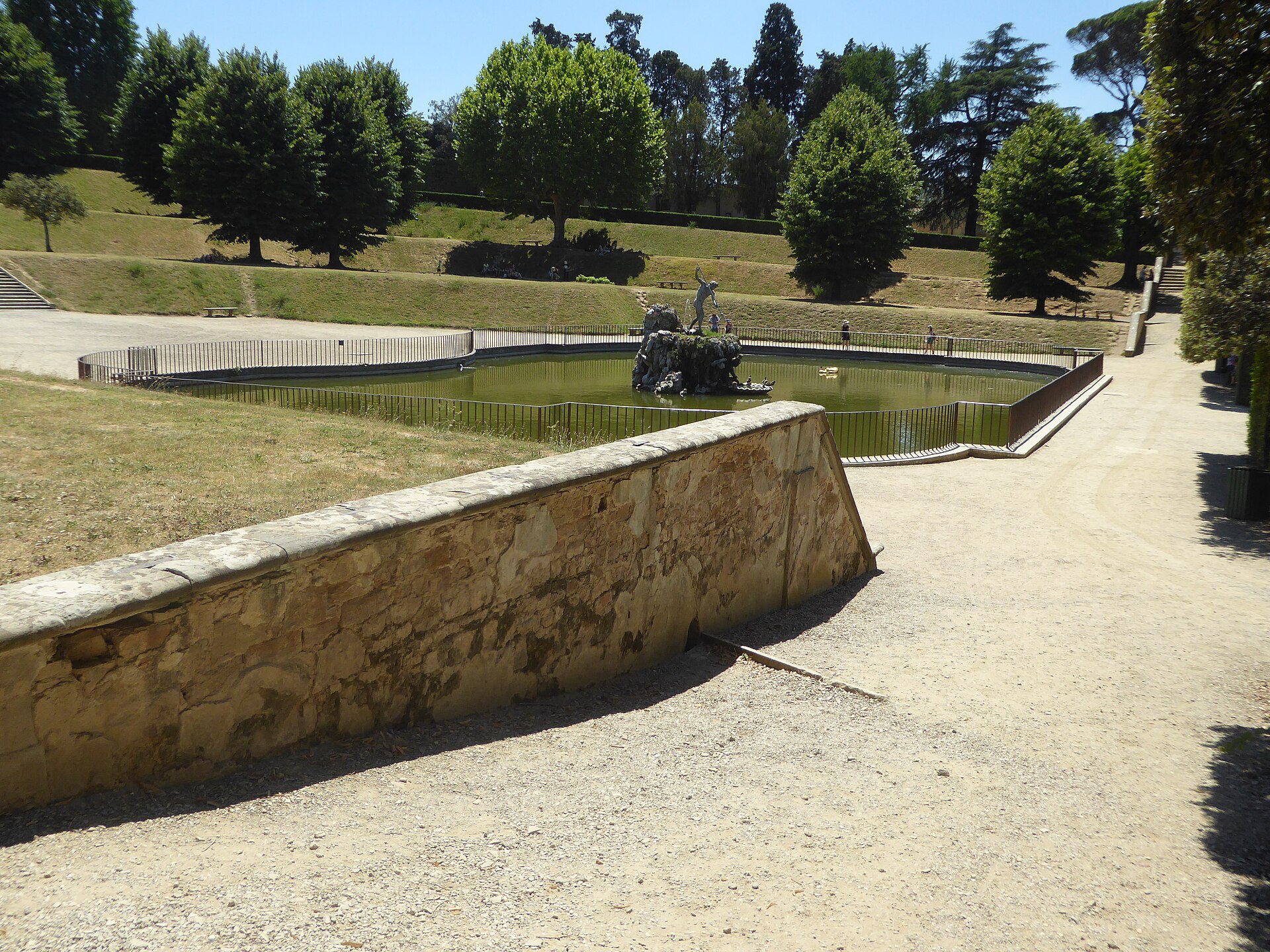 A formal pond with a fountain sculpture in the Boboli Gardens, seen from a raised stone path