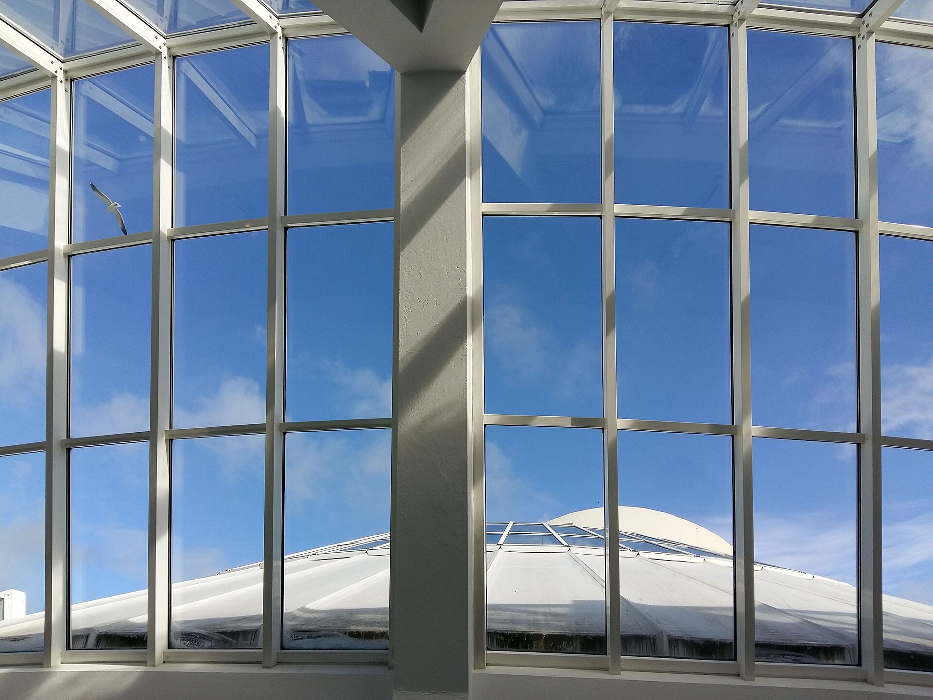 Looking up through a glazed link building toward the dome of Asmundarsafn from inside