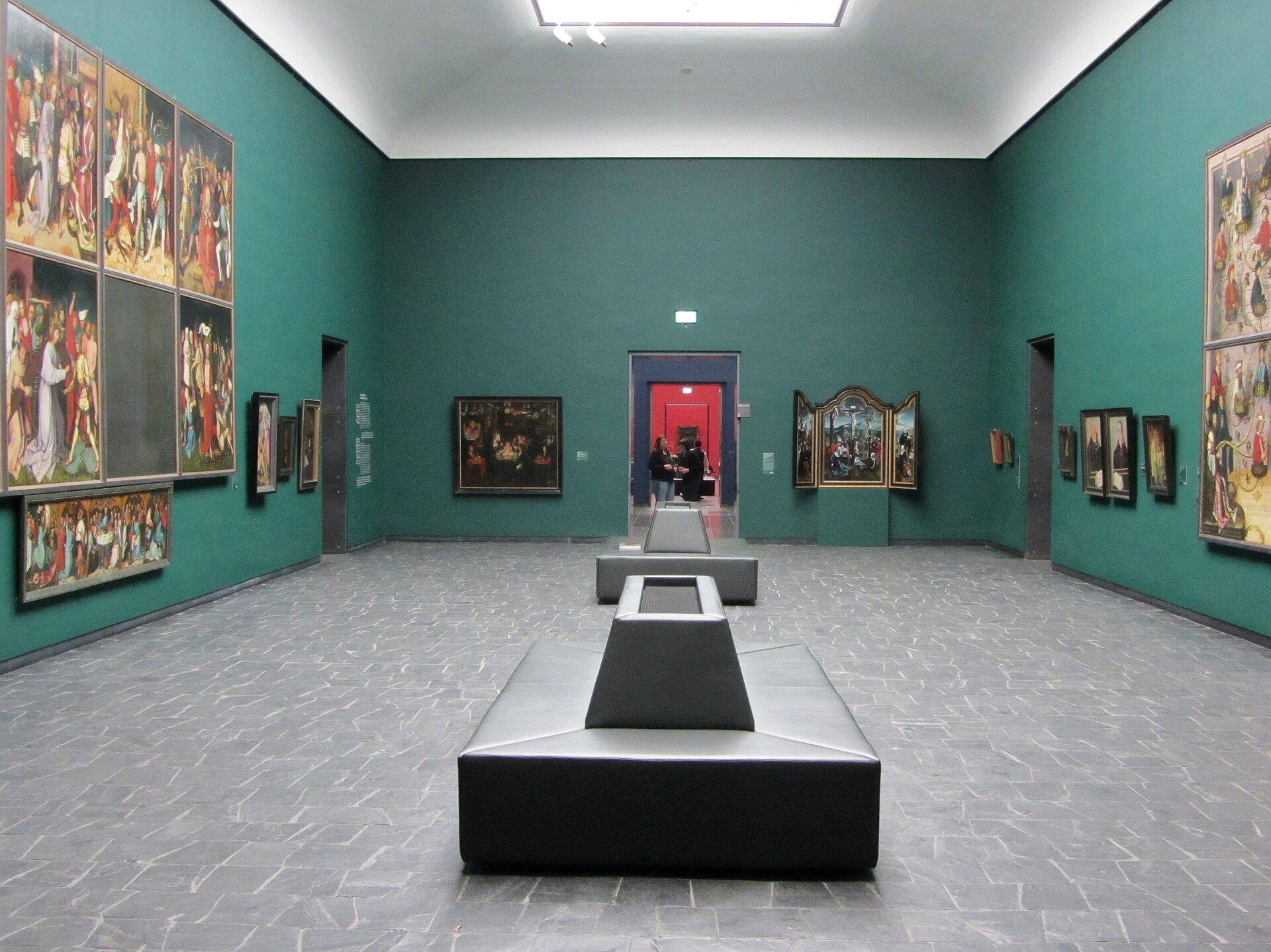 A gallery of the Old Masters collection, dark green walls hung with fifteenth-century Netherlandish altarpieces and panels