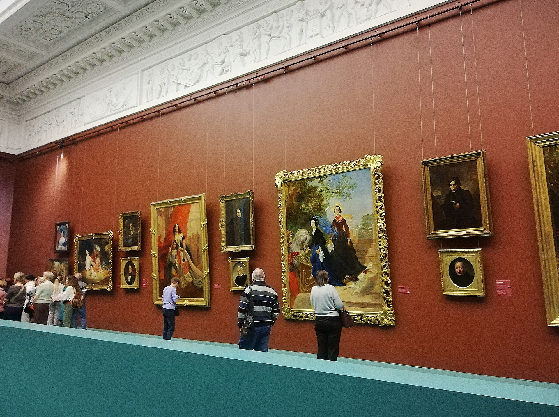 Visitors in a red-walled gallery hung with gilt-framed 19th-century portraits and paintings inside the Mikhailovsky Palace