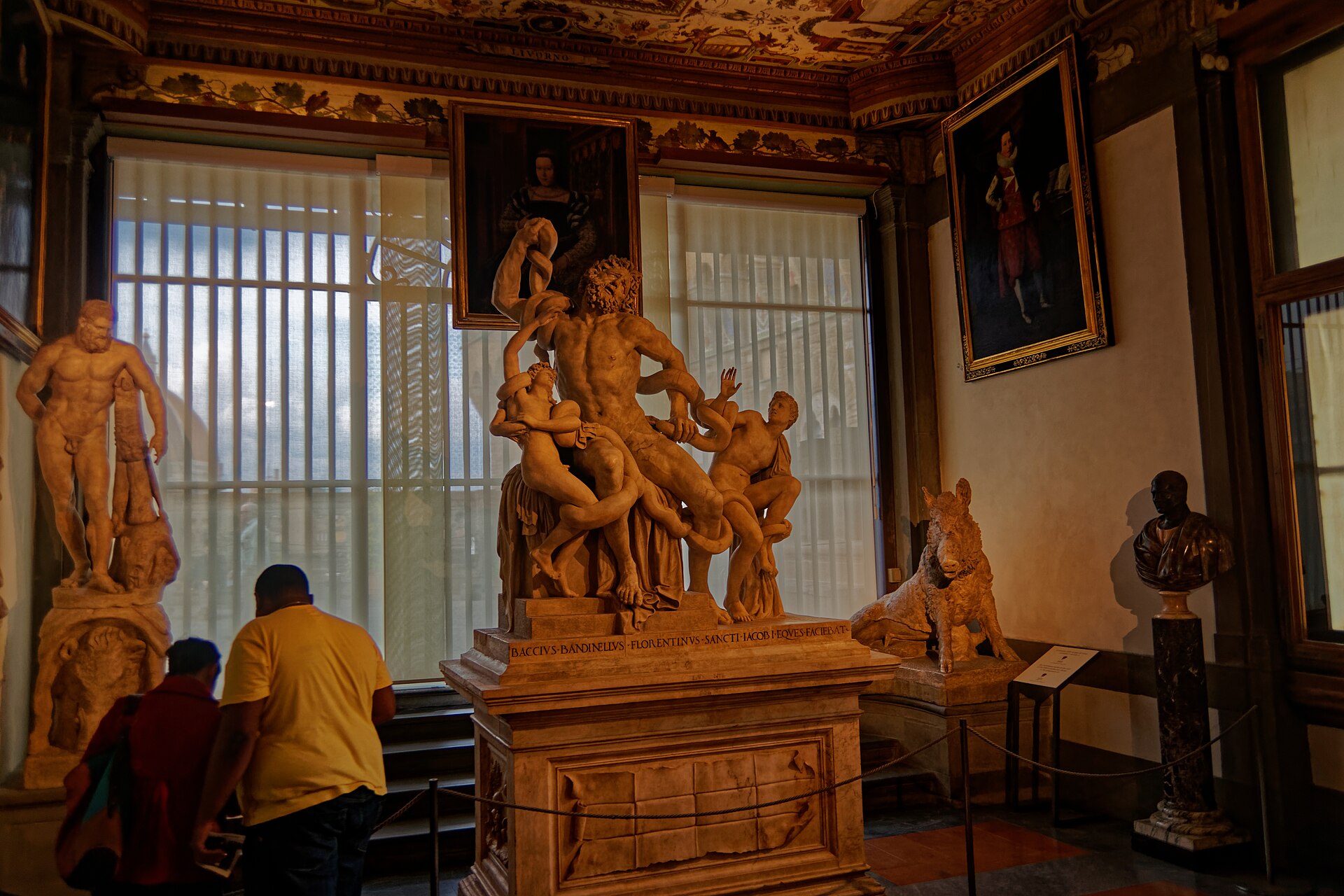 A gallery on the route of the Vasari Corridor, ancient statues along one side and tall windows overlooking Florence on the other