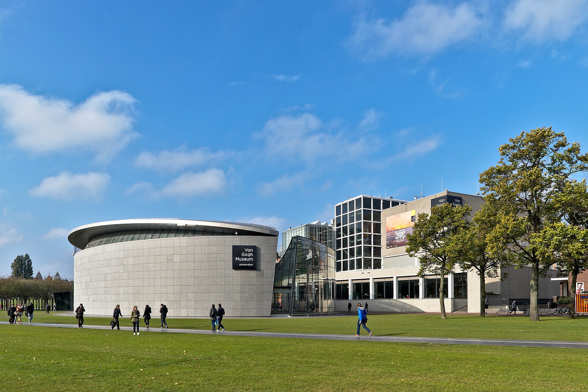 The drum-shaped stone exterior of the Kurokawa Wing and the glass entrance hall beside it, seen across Museumplein in daylight