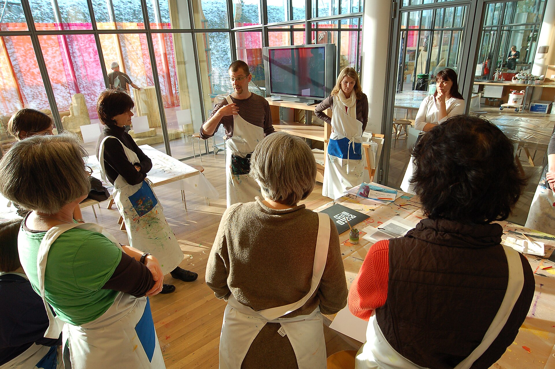 A group of adults in art smocks around a table during a Creaviva workshop at Zentrum Paul Klee